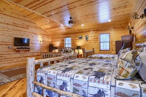 Interior d'una cabana de fusta amb un llit gran, una televisió i una llar de foc.