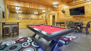 A pool table with a red felt surface, surrounded by bar stools and a patterned rug. - Freedom Lodge by Turkey Ridge Lodges (Rockbridge)