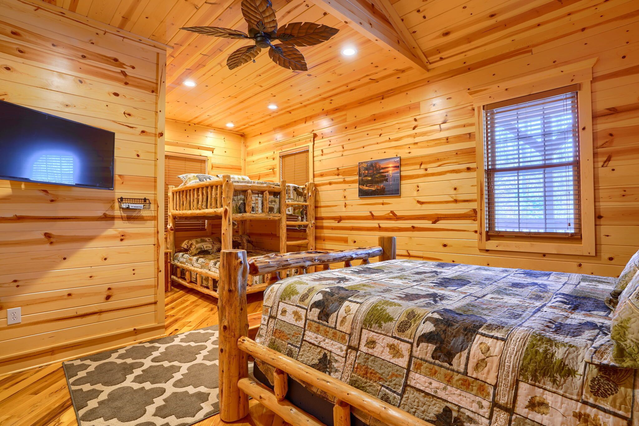 Une chambre dans un chalet en rondins, avec un lit superposé, un téléviseur à écran plat et une grande fenêtre.