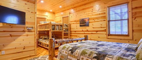 A log cabin bedroom with a bunk bed, a flat-screen TV, and a large window.