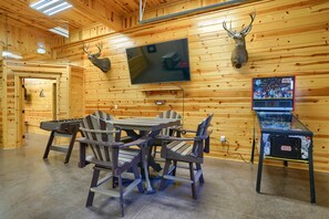 A wooden interior with a table and chairs, a mounted television, and a Star Wars arcade game.