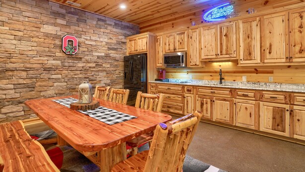 A wooden interior with a stone accent wall, a dining table with chairs, and wooden cabinets. - Freedom Lodge by Turkey Ridge Lodges (Rockbridge)