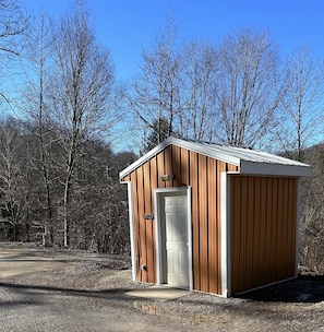 A small wooden shed with a white door and a small porch area. - Turkey Ridge Lodges- Cabin 10 (Rockbridge)
