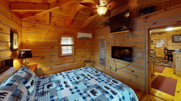 A cabin interior with a bed, a ceiling fan, a mounted TV, and a window.