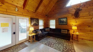 A log cabin interior with a wooden ceiling, a black leather couch, a mounted deer head, and a door with a check-out sign. - Turkey Ridge Lodges - Lodge # 2 (Rockbridge)