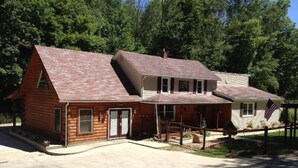 A two-story log cabin with a front porch, a garage, and a small attached shed. - Turkey Ridge Lodges - Lodge # 2 (Rockbridge)