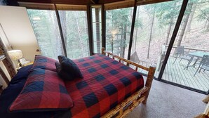 A bedroom with a large window, a bed with a quilt, a nightstand, and a lamp.