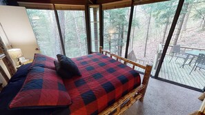 Une chambre avec une grande fenêtre, un lit recouvert d’une courtepointe, une table de chevet et une lampe.