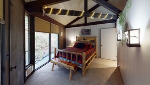 A bedroom with a wooden bed, a window with blinds, a door, and a wall-mounted light fixture.