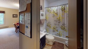 A bathroom with a toilet, sink, and shower curtain. There is a bulletin board with notices and a map on the wall.