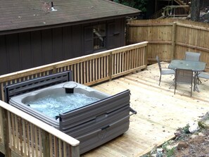 A hot tub on a wooden deck with a table and chairs nearby.