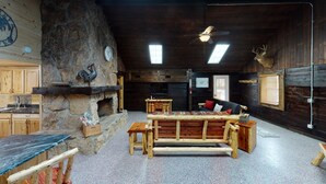 A rustic interior with a stone fireplace, wooden furniture, and a ceiling fan. - Turkey Ridge Lodges - The Nest (ROCKBRIDGE)