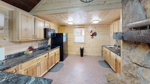 A compact kitchen with wooden cabinets, a black refrigerator, and a stone accent wall. - Turkey Ridge Lodges - The Nest (ROCKBRIDGE)