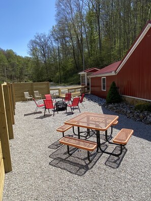 An outdoor patio area with a picnic table and red chairs, surrounded by a wooden fence and a red building. - Turkey Ridge Lodges - The Nest (ROCKBRIDGE)
