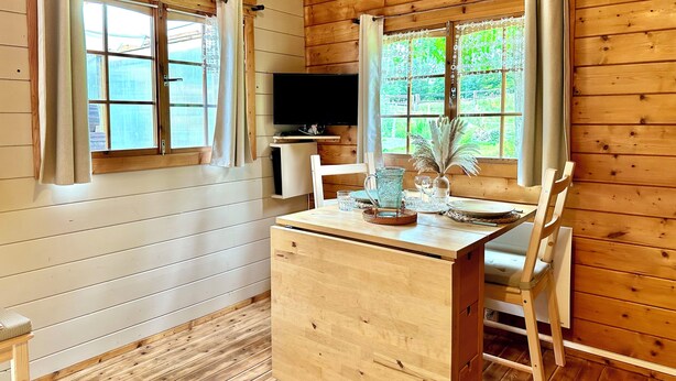 A wooden cabin with a wooden desk, two chairs, a television, and windows with curtains. - Chalet de la Prairie (Le Hom)