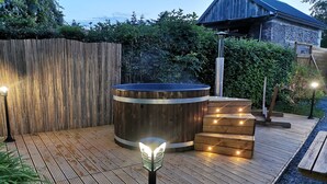A wooden deck with a hot tub, steps, and outdoor lighting. - Chalet de la Prairie (Le Hom)