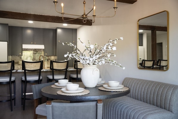Un comedor con una mesa redonda, sillas, un sofá, un jarrón con flores y un espejo en la pared.
