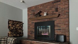 A living room with a brick fireplace, a sofa, and a television. - John & Anne`s Place LLC (Litchfield)