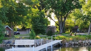 A dock extending into a calm body of water, surrounded by greenery and residential buildings. - John & Anne`s Place LLC (Litchfield)