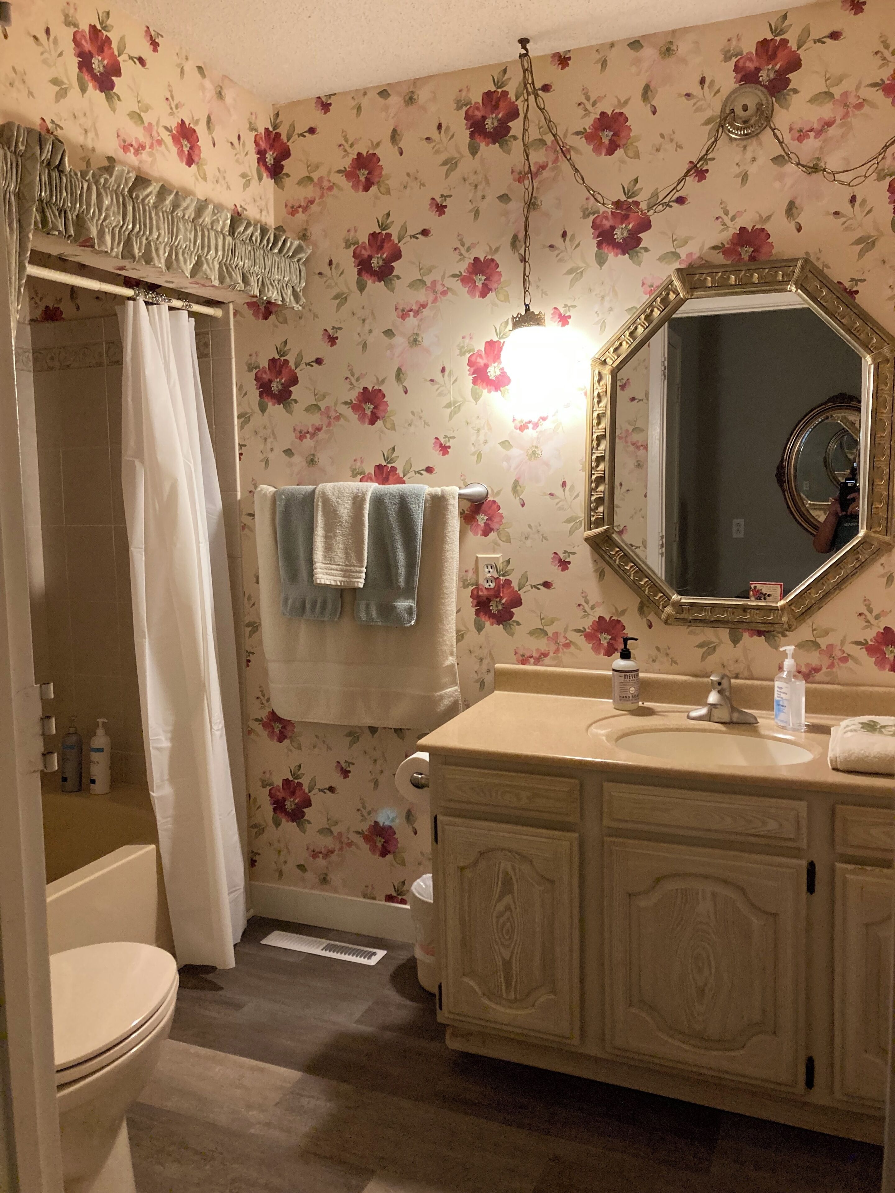 Un baño con papel tapiz floral, un tocador con espejo y una cortina de ducha.