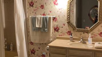 Un baño con papel tapiz floral, un tocador con espejo y una cortina de ducha.