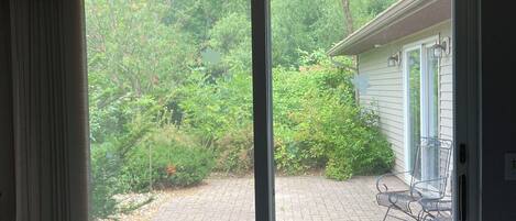 A room with a sliding glass door leading to a paved outdoor area with a patio chair and a small table.