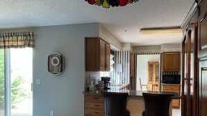 A kitchen with wooden cabinets, a microwave, and a dining area with two chairs. - John & Anne`s Place LLC (Litchfield)