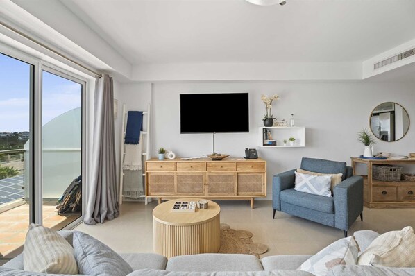 A modern living room with a flat-screen TV, a blue armchair, a wooden cabinet, and a round coffee table.