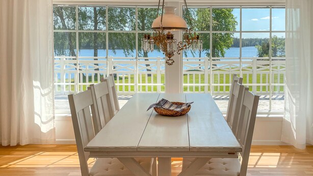 A dining area with a white table and chairs, a chandelier, and a view of a lake through large windows.