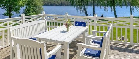 A deck with white furniture and a view of a lake.
