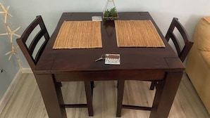 Una mesa de madera para comer con dos individuales tejidos, una pequeña planta en maceta y un llavero en el centro.