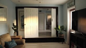 Una sala de estar con un sofá, una mesa de centro, un televisor y una puerta que da a otra habitación.