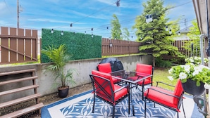 An outdoor patio with red chairs, a glass table, and a blue patterned rug. - Mighty Manor (North Battleford)