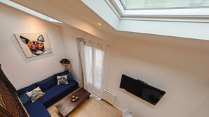 Un salón moderno con un sofá azul, una mesa de centro, un televisor montado en la pared y un tragaluz.