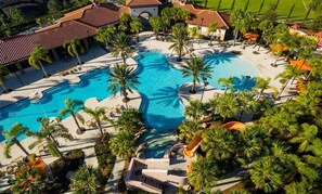 Vista aérea de un complejo turístico con una piscina central grande, varias piscinas más pequeñas y una variedad de palmeras.