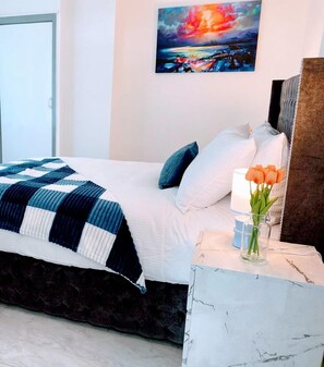 Una cama bien hecha con una colcha a rayas, una mesita de noche con un jarrón de flores y un cuadro en la pared.