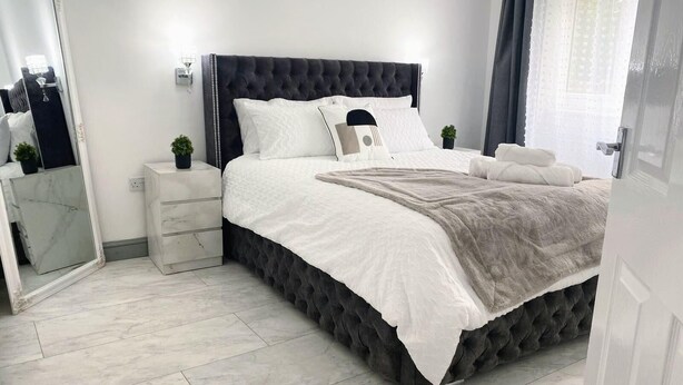 A modern bedroom with a large bed, a nightstand, a mirror, and a small plant.