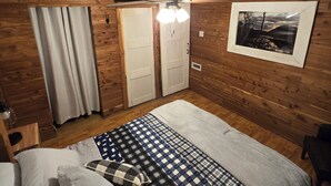 Un dormitorio con paredes de madera, una cama con colcha a cuadros, un ventilador de techo y un cuadro enmarcado en la pared.