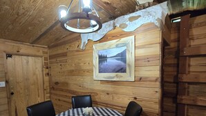 Una cabaña de madera acogedora con una mesa redonda y sillas, una araña y un cuadro en la pared.