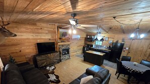 Interior acogedor de una cabaña con techo de madera, chimenea, comedor y sala de estar con sofás de cuero.