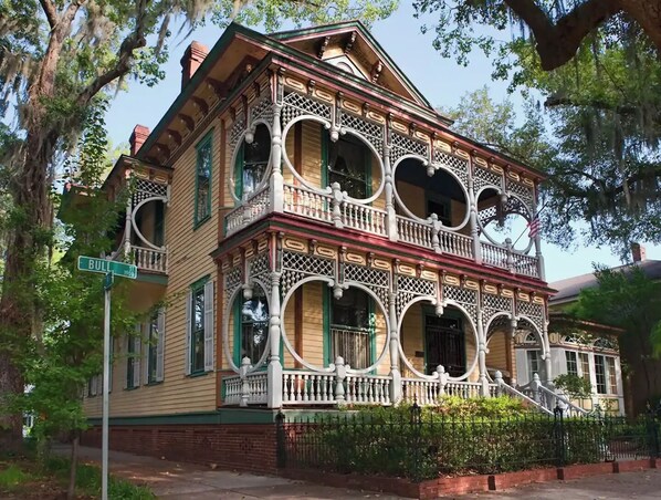 A historic two-story house with ornate balconies and a brick foundation.