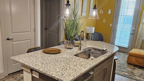Cocina con encimeras de granito, electrodomésticos de acero inoxidable e iluminación colgante.