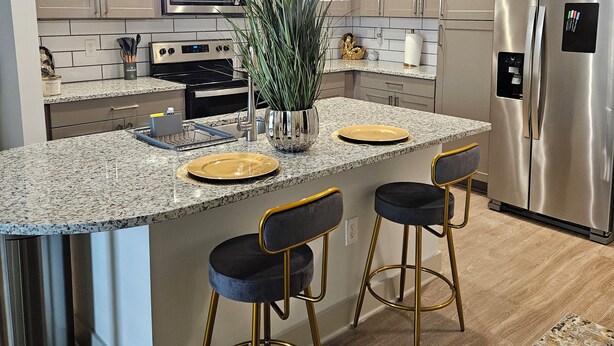 Una cocina moderna con encimeras de granito, electrodomésticos de acero inoxidable y taburetes de bar.