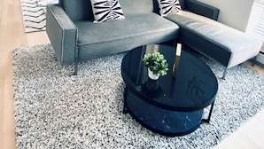 Un salon moderne avec un canapé gris, une table basse noire et un tapis à motifs.
