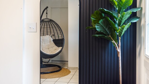 Un couloir avec un fauteuil suspendu, une plante en pot et une porte donnant sur une autre pièce.