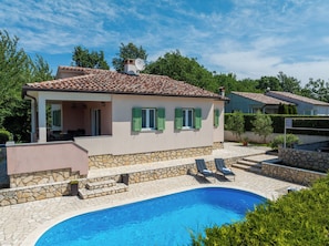 Une maison avec une piscine, des marches en pierre et des volets verts.
