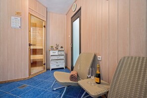 Una sauna con una porta in legno, un piccolo tavolo con una bottiglia e un bicchiere, e una sedia in vimini.