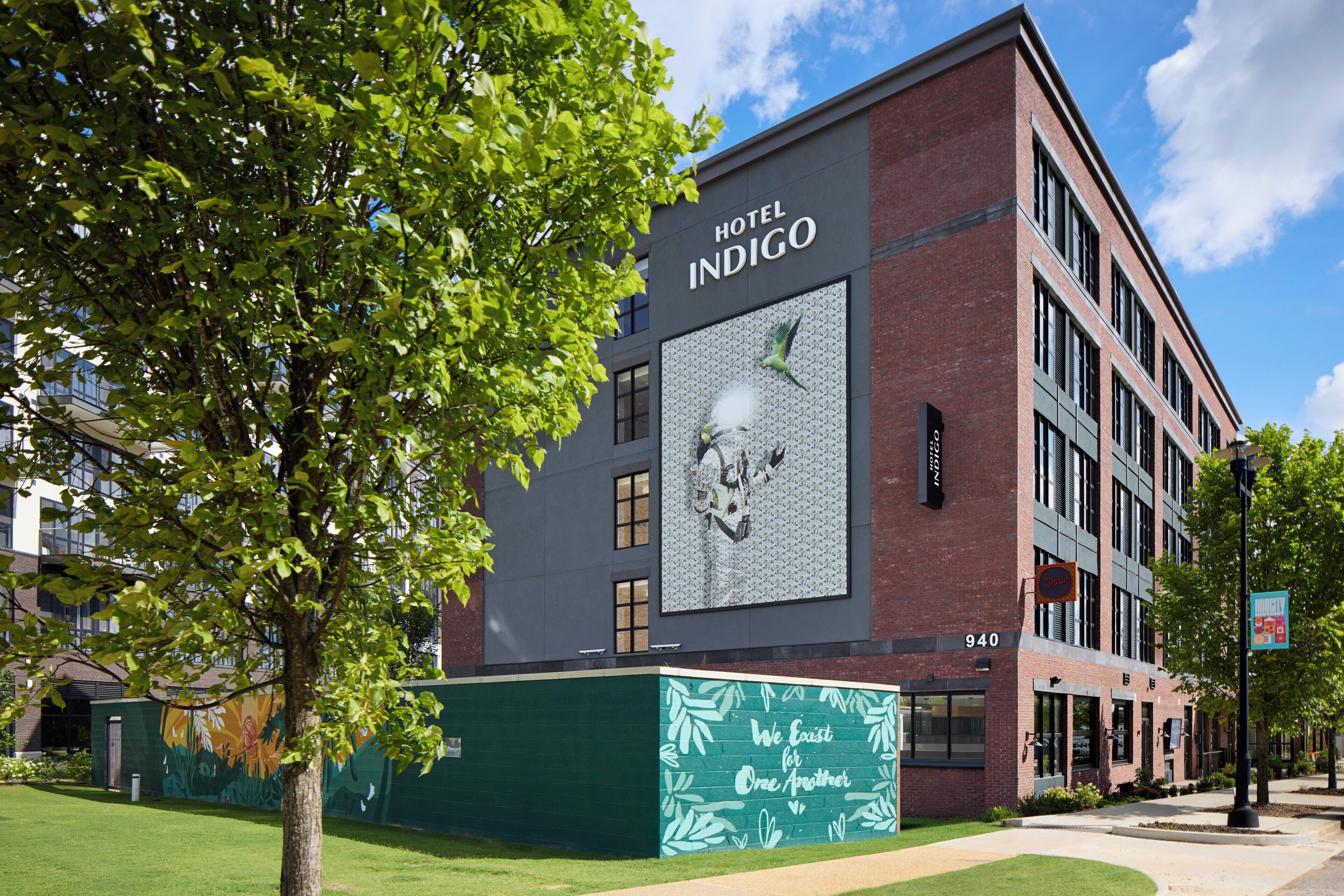 A building with a large mural on the side, a sign for 'Hotel Indigo', and a green sign with text.