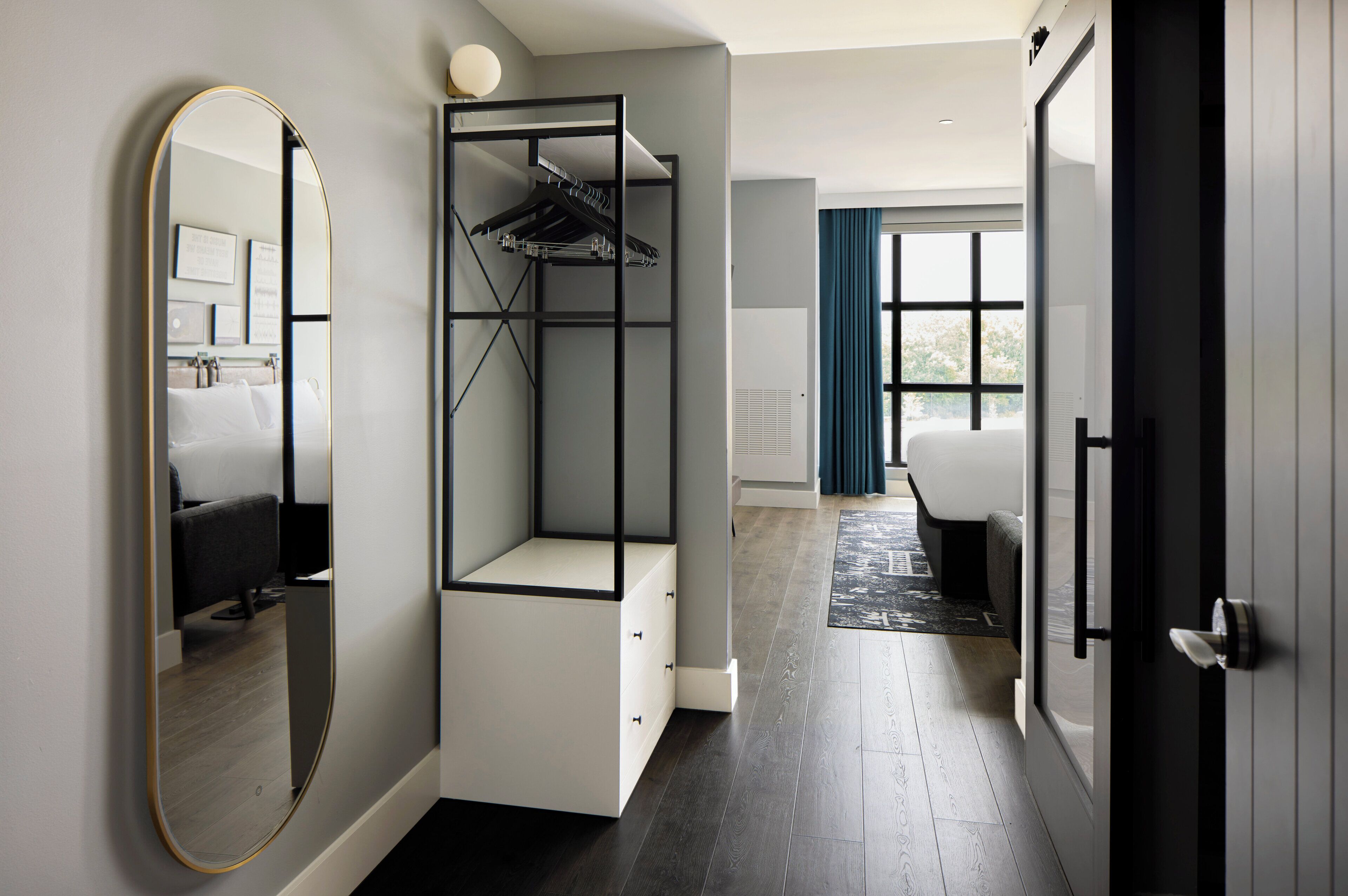 A modern hotel room with a walk-in closet, a large mirror, a bed, and a view of the outdoors.