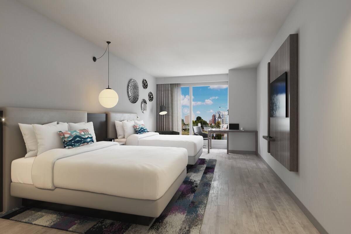 Ein modernes Hotelzimmer mit zwei Betten, einem Schreibtisch und einem großen Fenster mit Blick auf die Stadt.